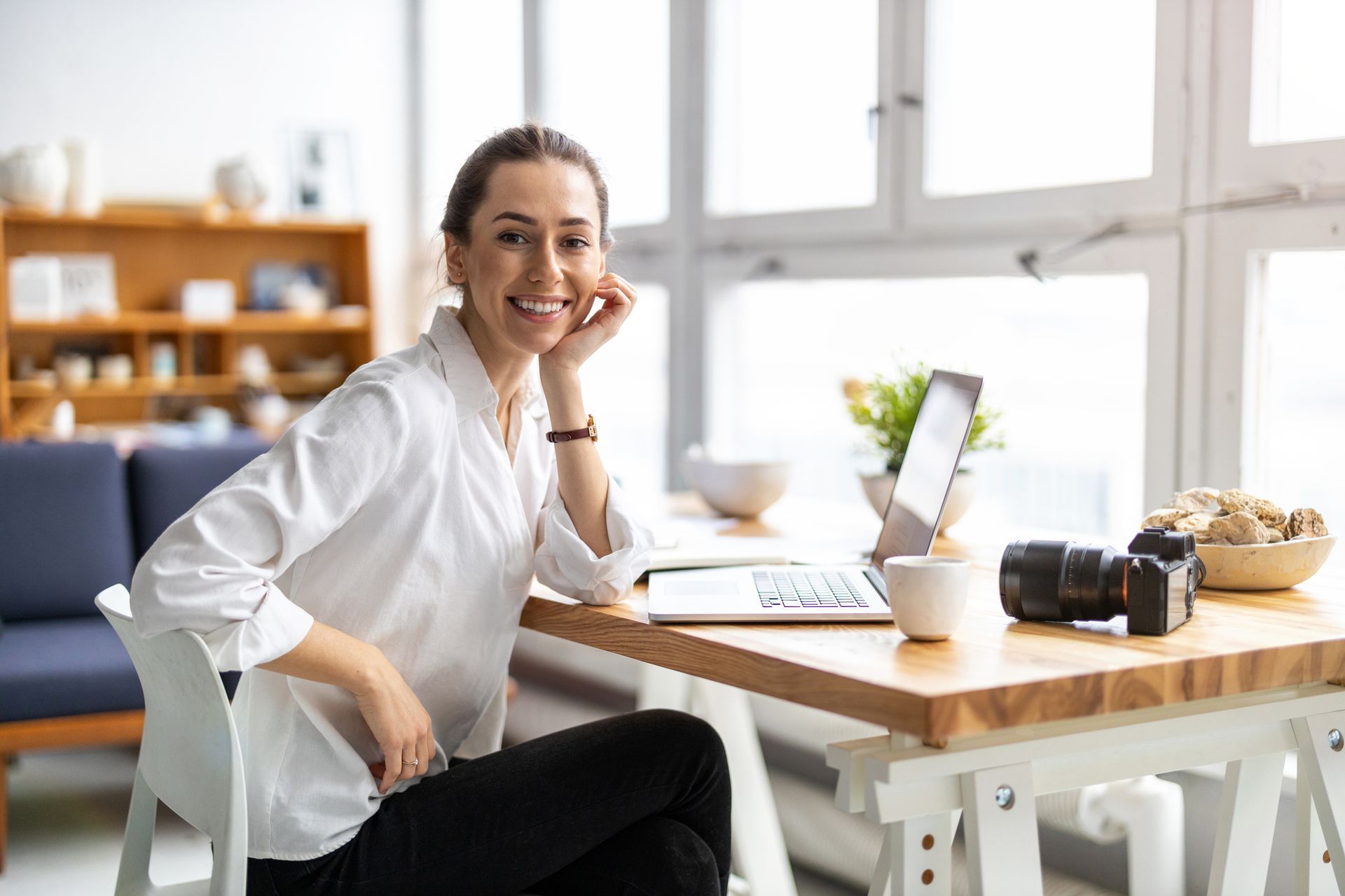 A woman is sitting at a table with a laptop and a camera.