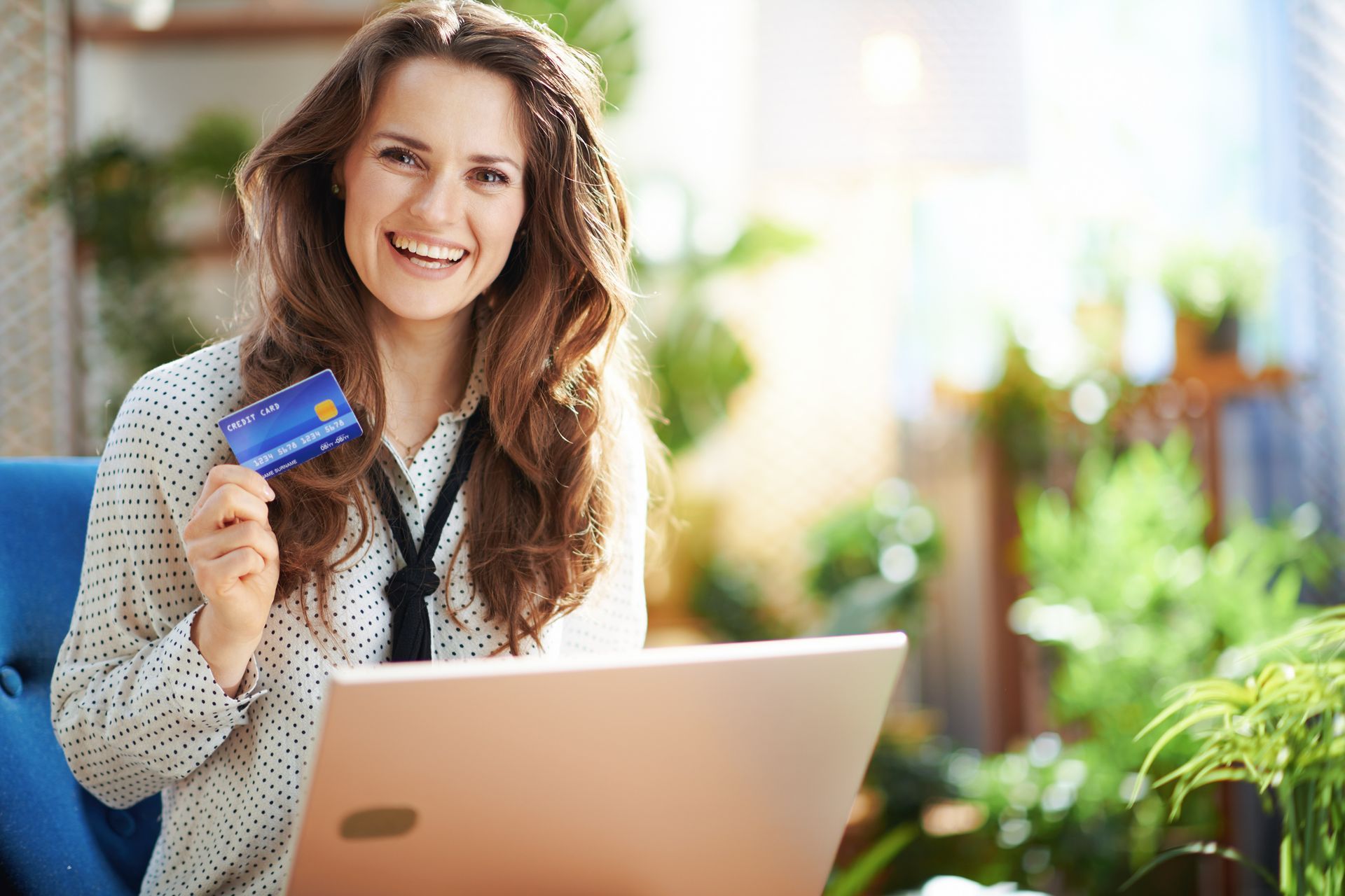 A woman is holding a credit card while using a laptop computer.