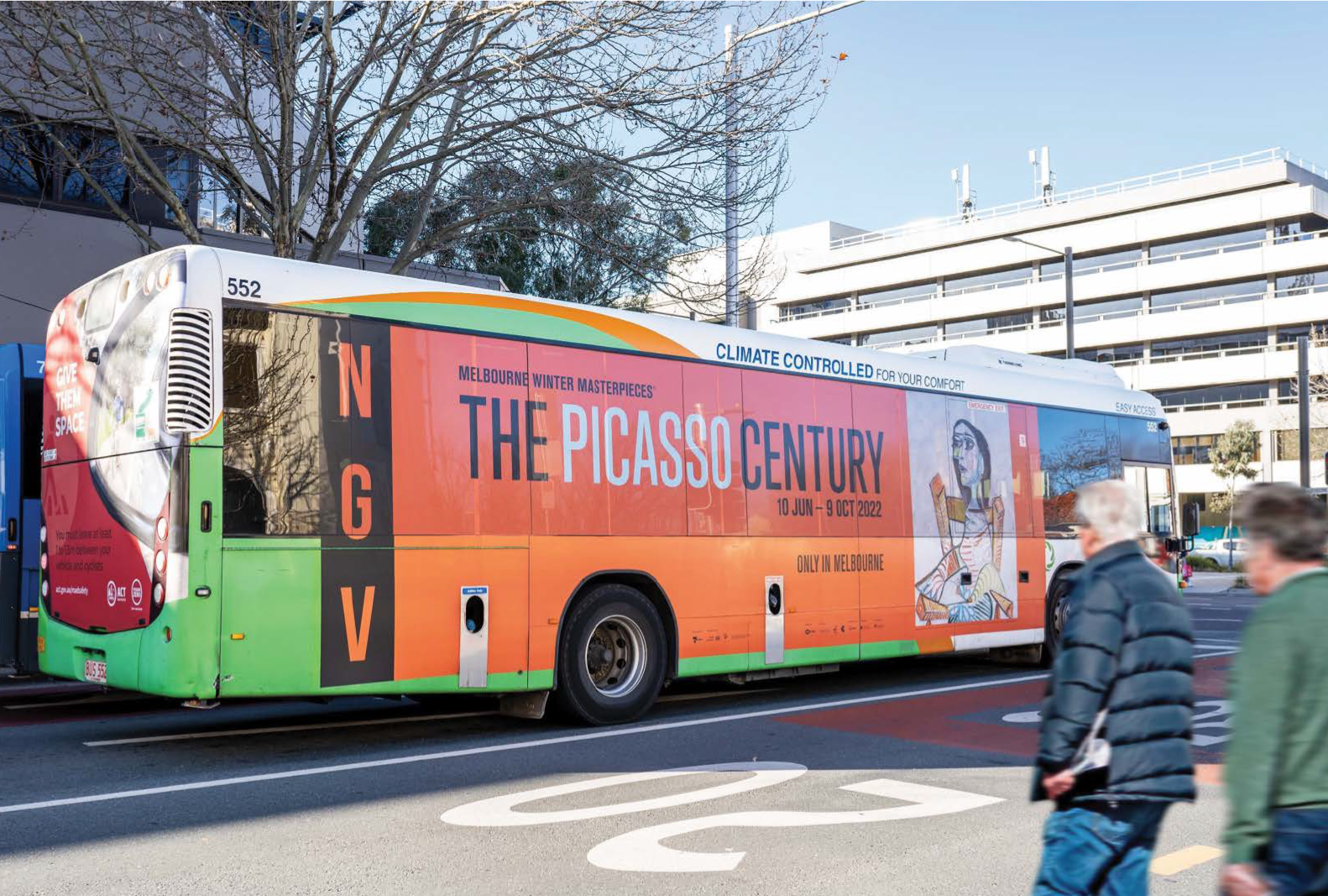 A green and orange bus is parked on the side of the road.