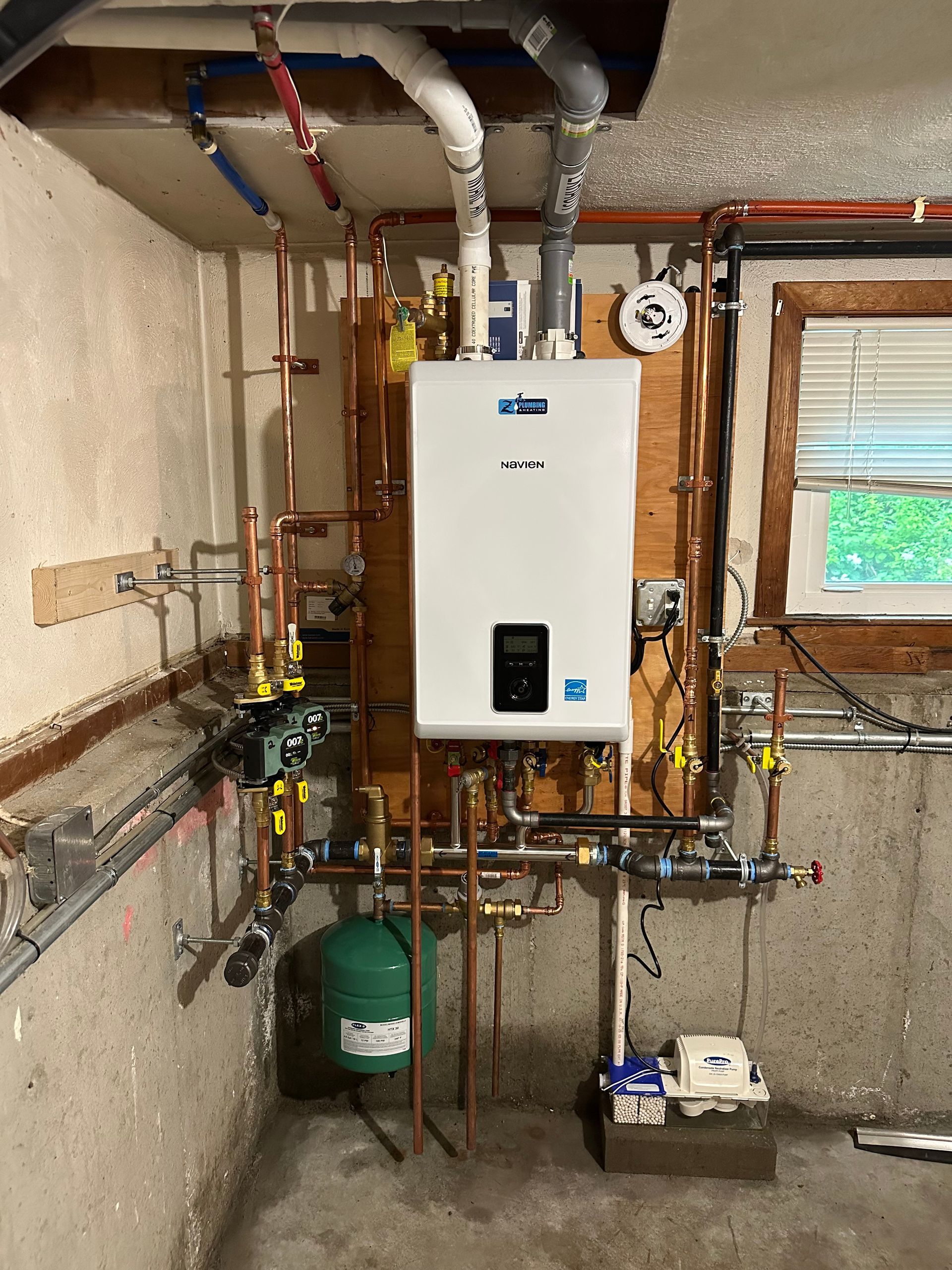 A gas-powered water heater installed on a wall in a basement, with associated copper pipes and fittings.