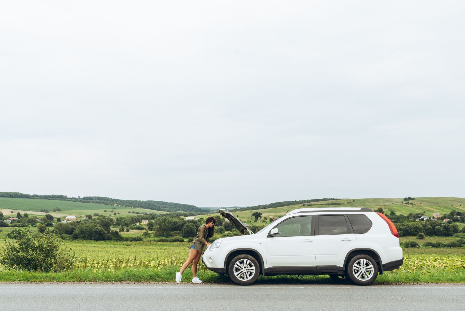 A woman is standing at a roadside with a broken car.