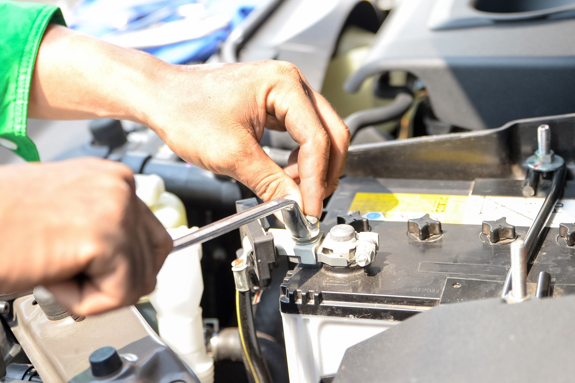 Close-up of hands while they fit a car’s battery screws, securing it to a car’s hood. 
