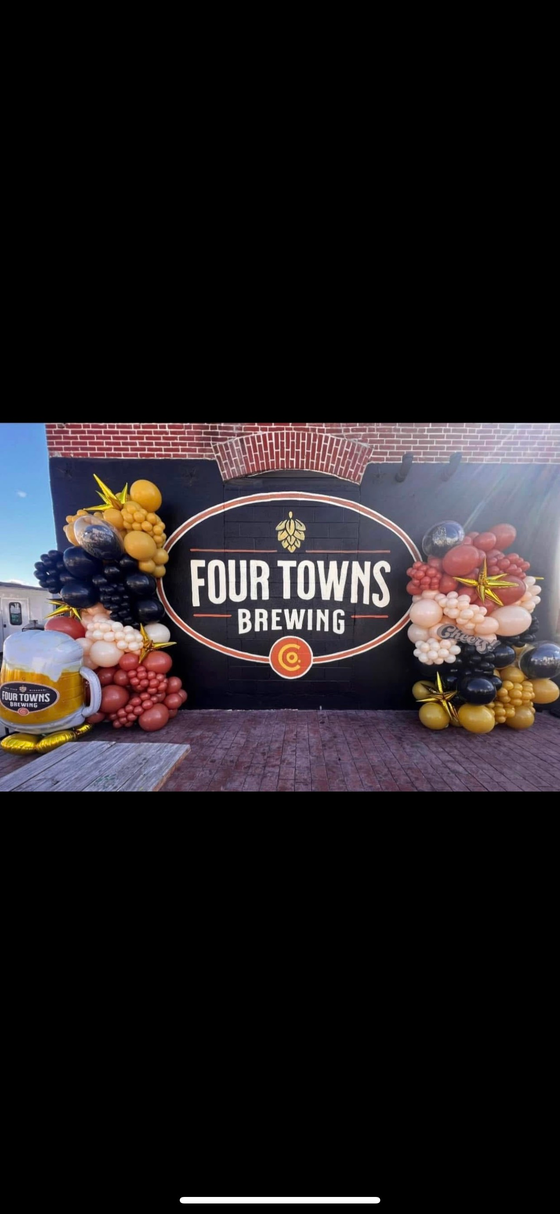 A sign for four towns brewing is surrounded by balloons.