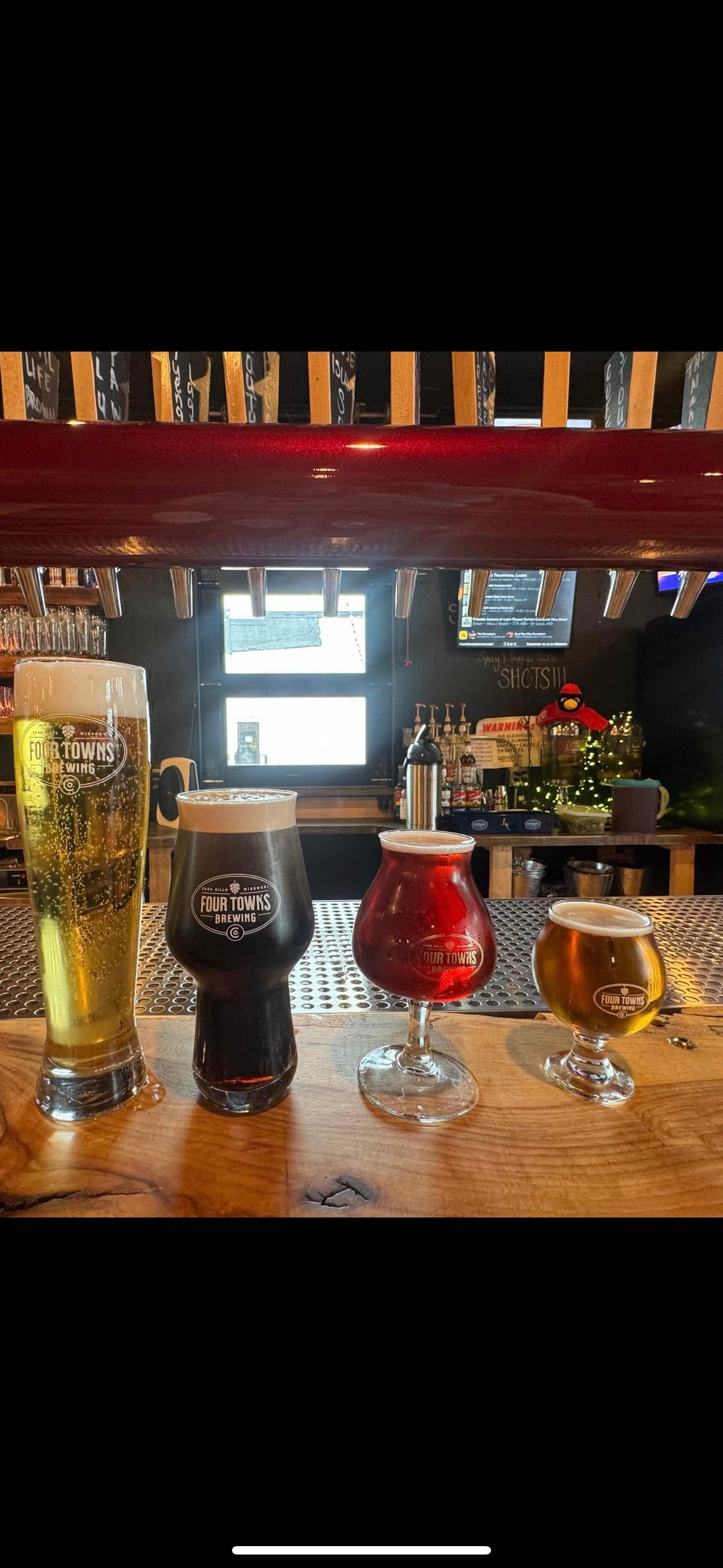 Four glasses of beer are sitting on a bar.