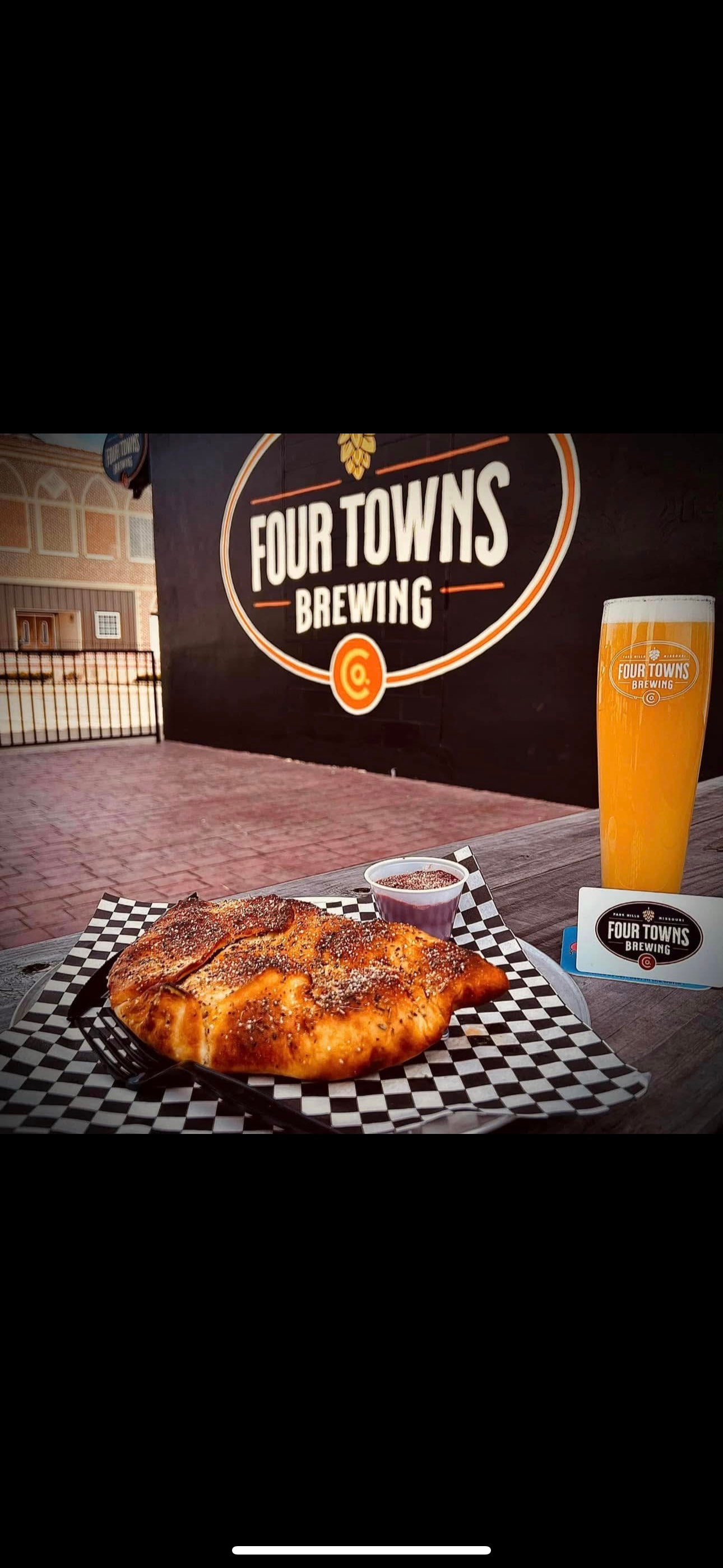 A pizza and a glass of beer are on a table in front of a four towns brewing sign.