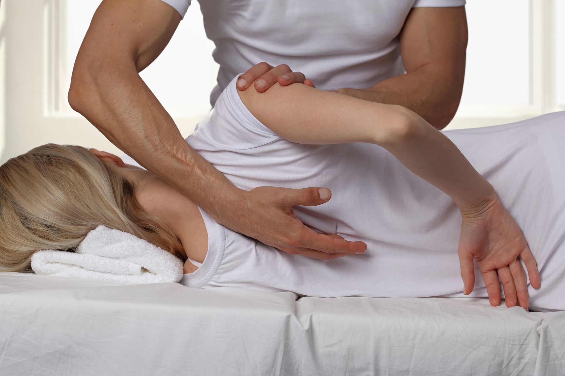 Therapist supporting a person lying on a table while guiding an arm stretch.