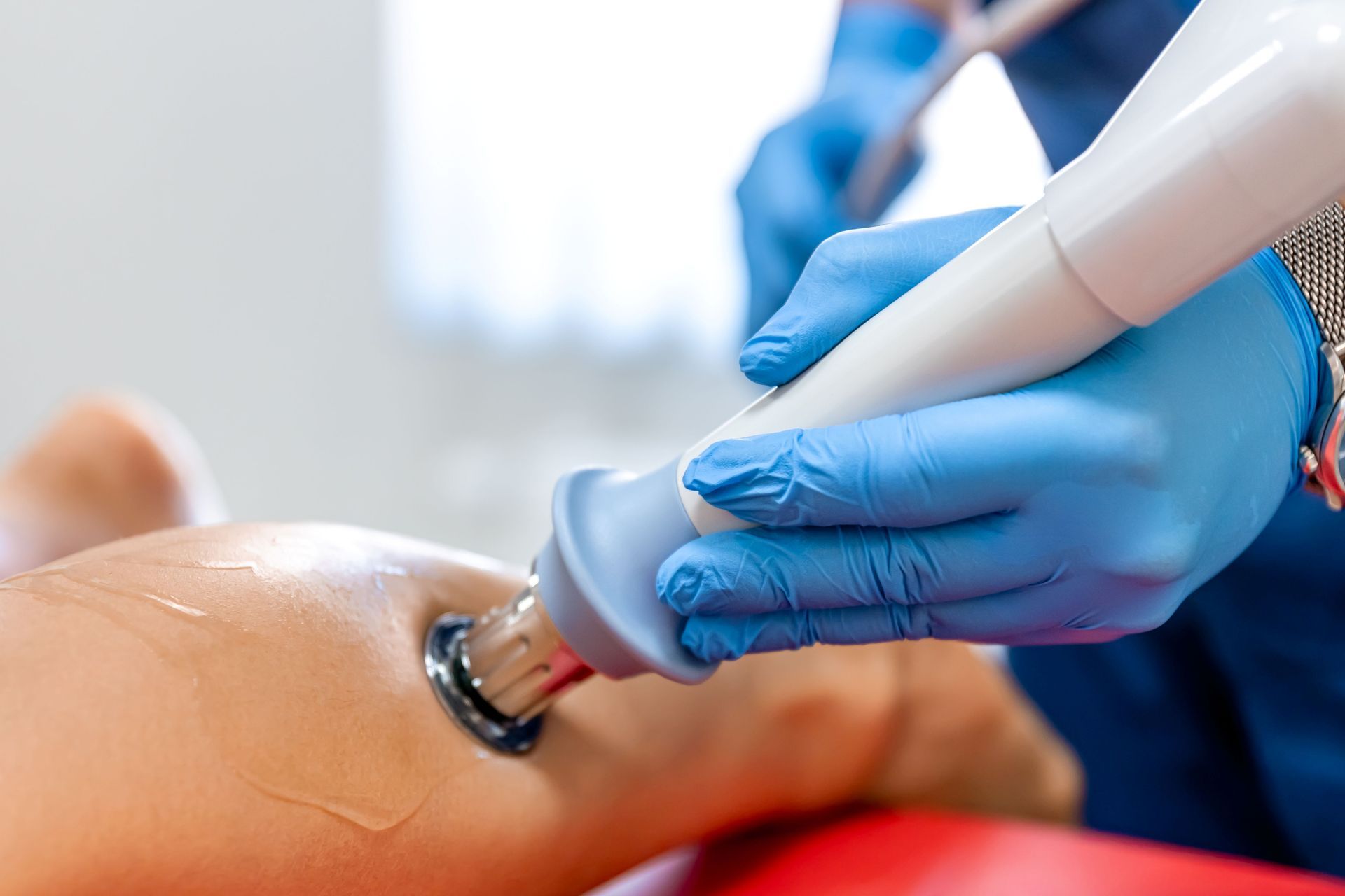 A gloved professional uses an ultrasound therapy wand on a patient's leg, which is covered in conductive gel.