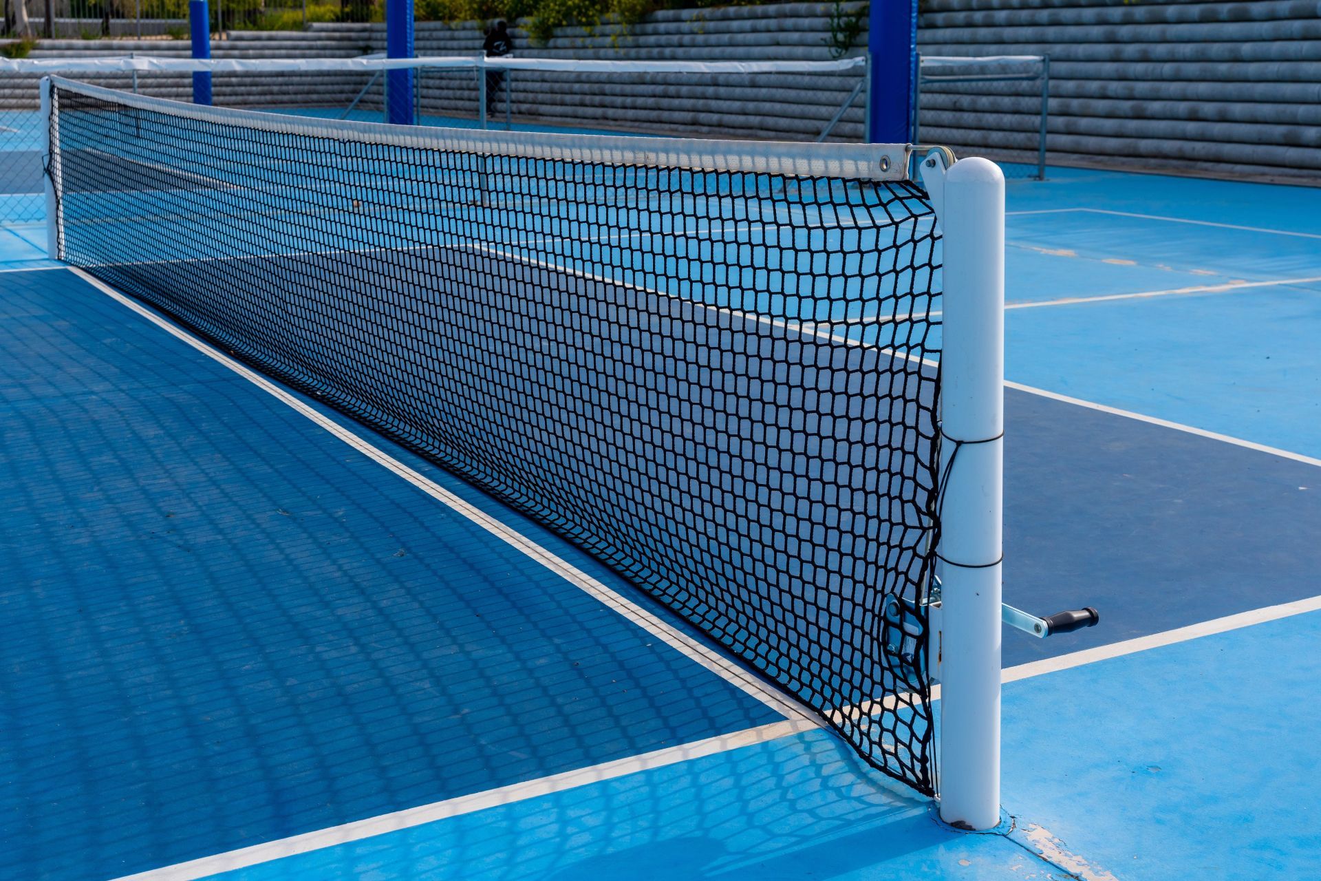 Pickleball net on a blue outdoor court with white posts and markings
