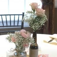 Two small pink-flower arrangements in glass vases on a table by a window with a boat visible outside
