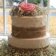 Two-tier white cake with pink rose topper and baby's breath decorations by a window