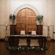 Decorated wedding altar with arched wooden doors, white drapery, candles, and floral arrangements
