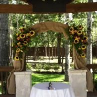 Sunflower-adorned wedding arch in an outdoor pavilion with a small table in front