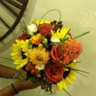 Handheld bouquet of orange, yellow, and peach flowers with green accents