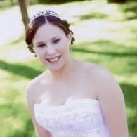 Smiling bride in a strapless white dress outdoors with a blurred green background