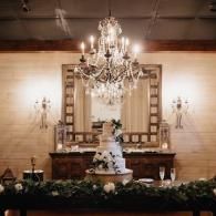 Elegant wedding cake on a decorated table beneath a chandelier in a warmly lit reception hall