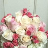 A bouquet of white and pink roses with green leaves against a light background