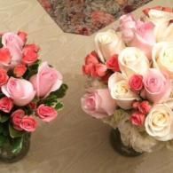 Two bouquets of pink and white roses in glass vases on a beige table.