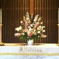 Floral arrangement on a church altar with white cloth and gold trim, against a dark wooden backdrop