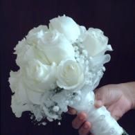 White bridal bouquet with roses and baby's breath held in a hand against a dark background