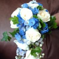 Blue and white flower bouquet with green leaves against a dark background