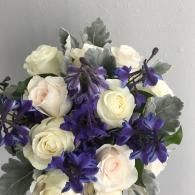 Bouquet of white roses and purple flowers with gray-green leaves against a light wall