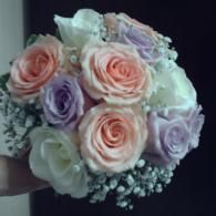 Bouquet of pale pink, white, and lavender roses with baby's breath on a dark background