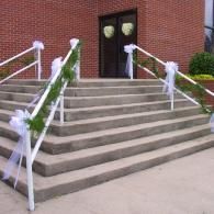 Wide concrete stairs leading to a brick building entrance with white railings and green garlands
