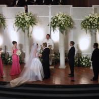 Wedding ceremony on a stage with bride, groom, officiant, and floral arrangements behind them