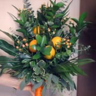 Bouquet of green foliage with yellow flowers and orange fruit in a vase
