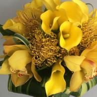 Yellow calla lilies and textured golden flowers arranged in a bouquet with green leaves