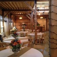 Rustic banquet hall with round tables, floral centerpieces, and warm wooden beams