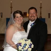 Bride and groom smiling in a church, holding a bouquet of white and purple flowers