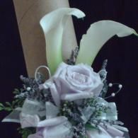 White floral bouquet with calla lilies, lavender roses, and silver greenery on a dark background