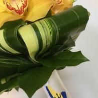 Close-up of a green-wrapped floral bouquet with yellow flowers and dark green leaves