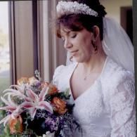 Bride in a white dress and veil holding a bouquet of pink and orange flowers by a window
