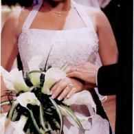 Person in a white lace dress holding a black-and-white bouquet and a folded paper.
