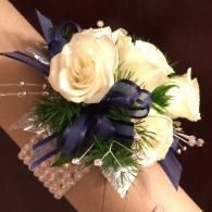 White rose corsage with navy ribbon and pearl accents on a wrist
