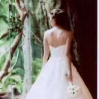 Bride in a white gown standing with her back to the camera among lush green foliage.
