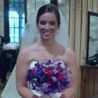 Bride holding a purple and white bouquet, smiling in a white dress and veil indoors