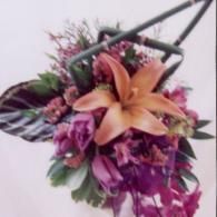 Purple and orange floral arrangement with green leaves and dark ribbon on a white background
