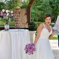 Bride in white dress holding a purple bouquet at an outdoor wedding reception booth