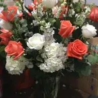 Bouquet of coral and white roses with white filler flowers and greenery in a box