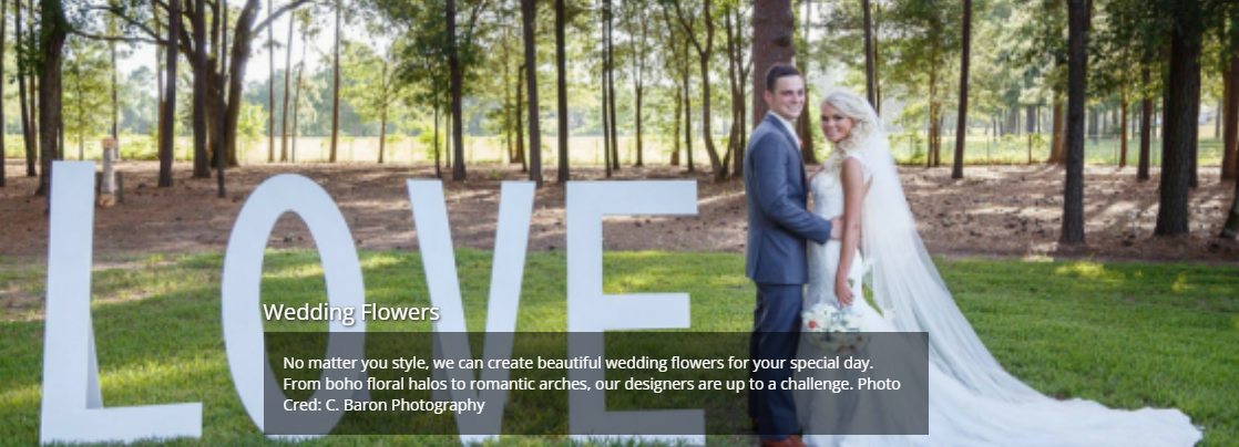 Bride and groom standing by large white “LOVE” letters in a wooded outdoor setting