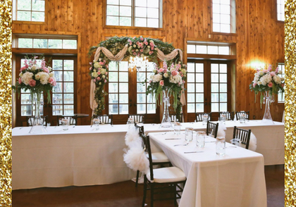 Elegant banquet hall with white table settings, floral arch, and tall windows in warm wood-paneled room