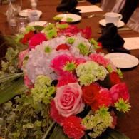 Pink and white floral centerpiece on a dining table with plates and cups in the background