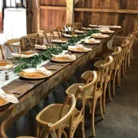 Long wooden dining table set with white plates and wicker chairs in a rustic barn-like room