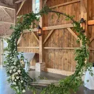Floral wedding arch in a rustic barn with wooden doors and white flower arrangements
