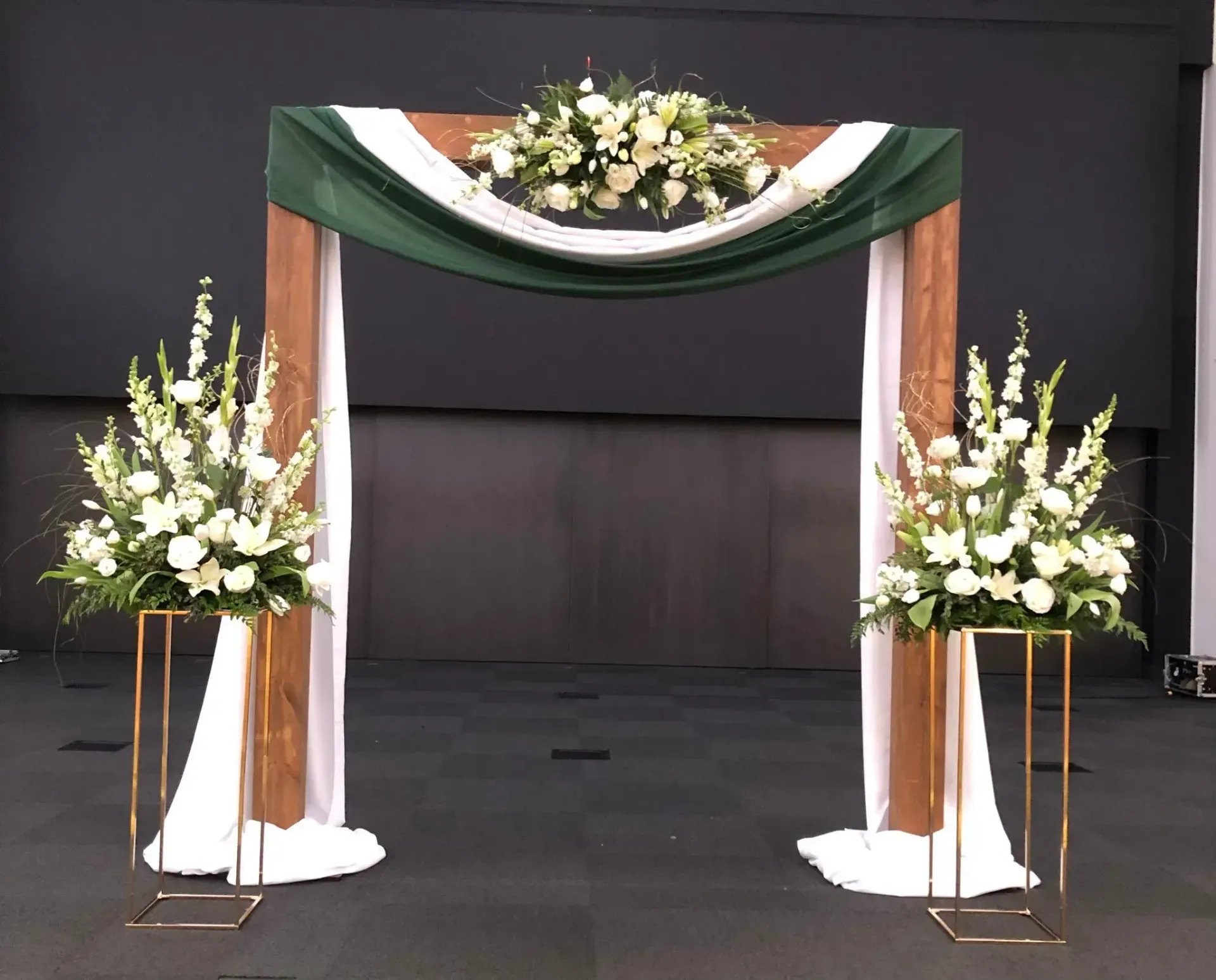 Floral funeral arch with white flowers and green drapery on a dark stage