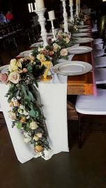 Decorated banquet table with white plates, lavender napkins, and cascading floral greenery centerpiece