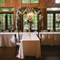 Decorated wedding reception table with floral arch and white linens in a rustic room